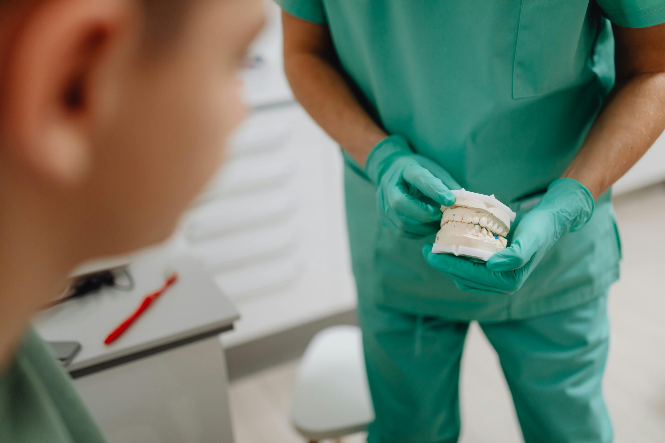 Dentist in green scrubs holding a dental mold during patient consultation in clinic.